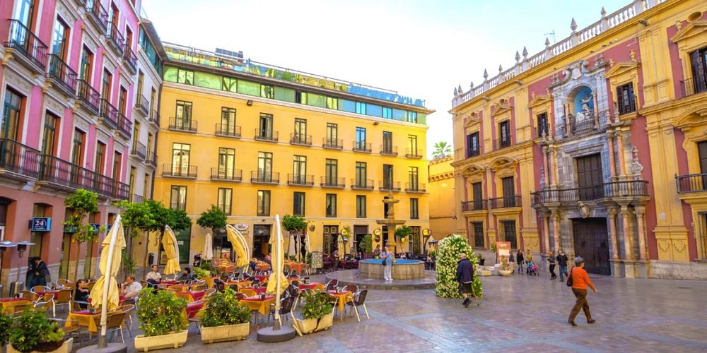 A bustling street in Centro Histórico, Malaga, with historic buildings lining the sides and people walking around, enjoying the vibrant atmosphere.